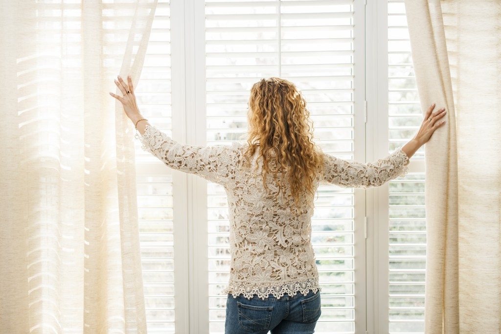 woman opening the curatin over the window blinds