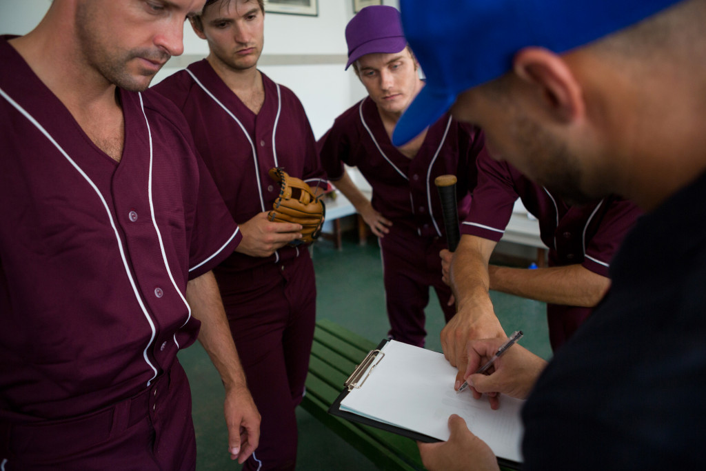 baseball coach writing plan on a paper while the team encircles him