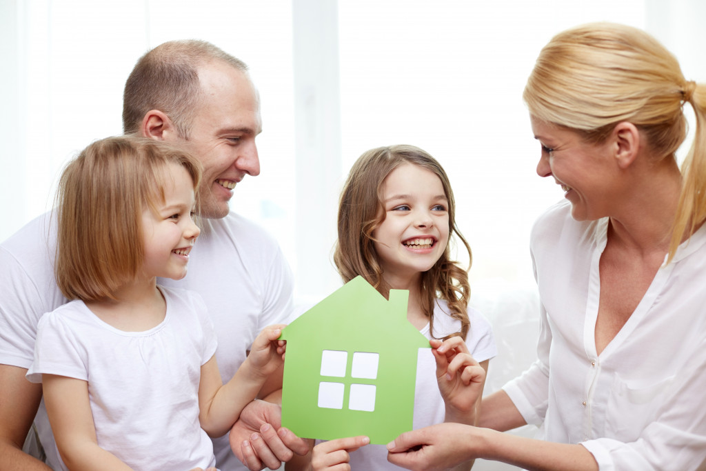 Concept of an eco-friendly home. A happy family holding a green cardboard cut-out of a house
