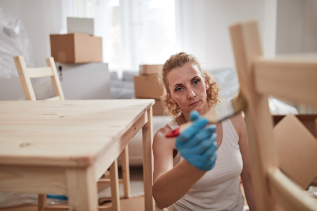 Woman painting a wooden chair in new apartment